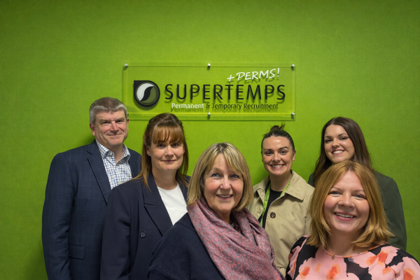 6 supertemps employees smiling for the camera on green background with Supertemps logo