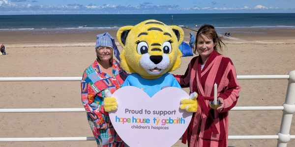 Two ladies in pyjamas and fun tiger on beach with Ty Gobaith sign