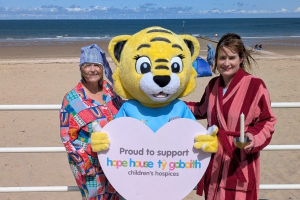 Two ladies in pyjamas and fun tiger on beach with Ty Gobaith sign